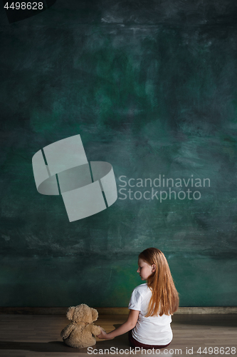 Image of Little girl with teddy bear sitting on floor in empty room. Autism concept