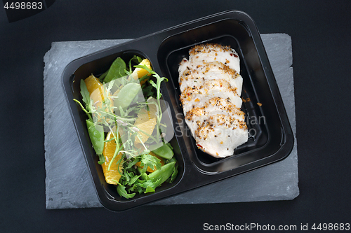 Image of Balanced box diet, dinner dish. Poultry fillet on a salad with sugar peas and oranges on a black plate.