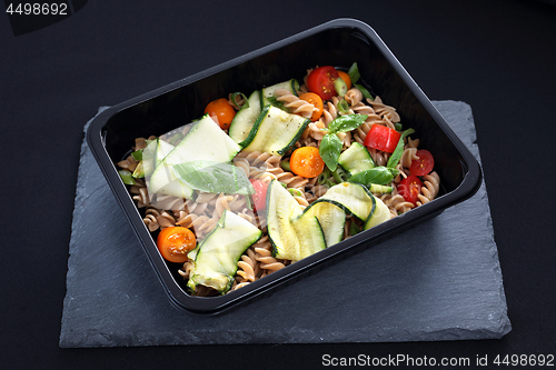 Image of Dietary catering. Pasta salad with zucchini and tomatoes served on a black plate.