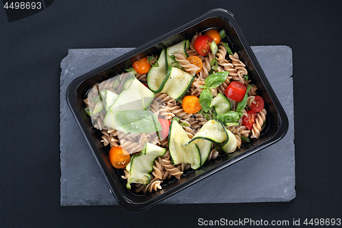 Image of Box diet. Pasta salad with zucchini and tomatoes served on a black plate.