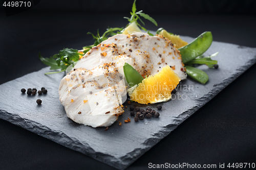 Image of Poultry fillet on a salad with sugar peas and oranges on a black plate.