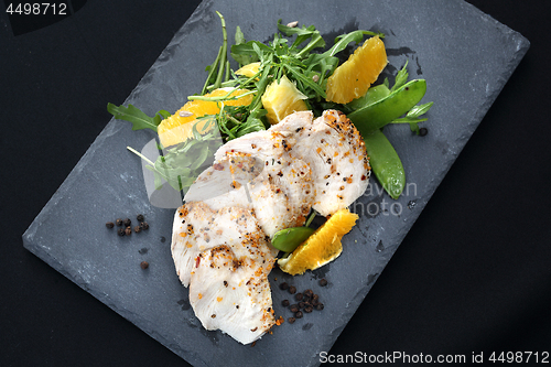 Image of Poultry fillet on a salad with sugar peas and oranges on a black plate.