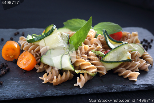 Image of Pasta salad with zucchini and tomatoes served on a black plate.