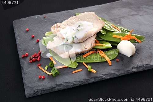 Image of Cooked meat on a sweet pea salad served with white yoghurt sauce.