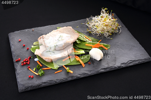 Image of Cooked meat on a sweet pea salad served with white yoghurt sauce.