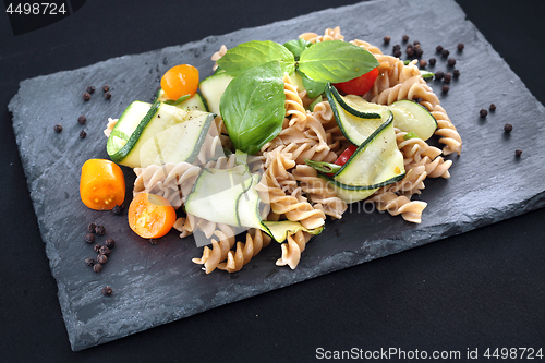 Image of Spiral pasta with vegetables. Pasta salad with zucchini and tomatoes served on a black plate.