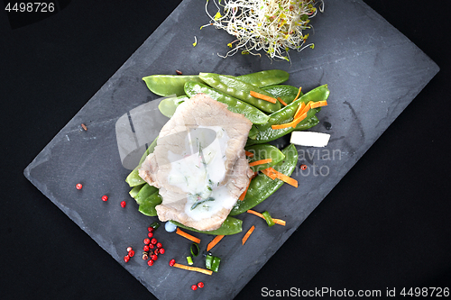 Image of Cooked meat on a sweet pea salad served with white yoghurt sauce.