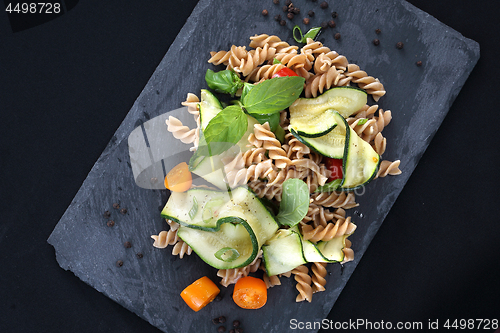 Image of Pasta salad with zucchini and tomatoes served on a black plate.