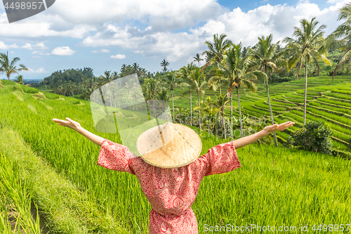 Image of Relaxed fashionable caucasian woman wearing red asian style kimono and traditional asian paddy hat, arms rised to sky, enjoying pure nature at beautiful green rice fields on Bali island