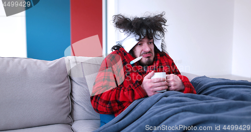 Image of sick man is holding a cup while sitting on couch