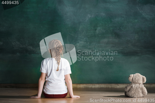 Image of Little girl with teddy bear sitting on floor in empty room. Autism concept