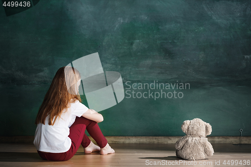 Image of Little girl with teddy bear sitting on floor in empty room. Autism concept