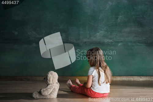 Image of Little girl with teddy bear sitting on floor in empty room. Autism concept