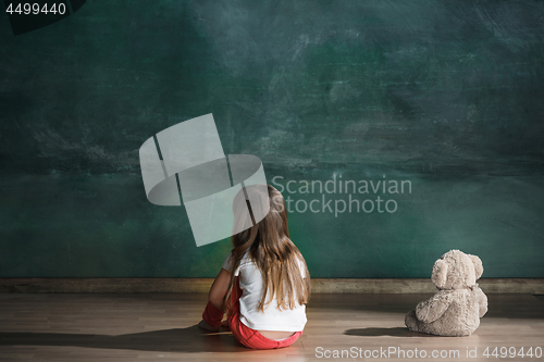 Image of Little girl with teddy bear sitting on floor in empty room. Autism concept