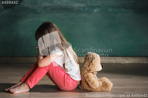 Image of Little girl with teddy bear sitting on floor in empty room. Autism concept