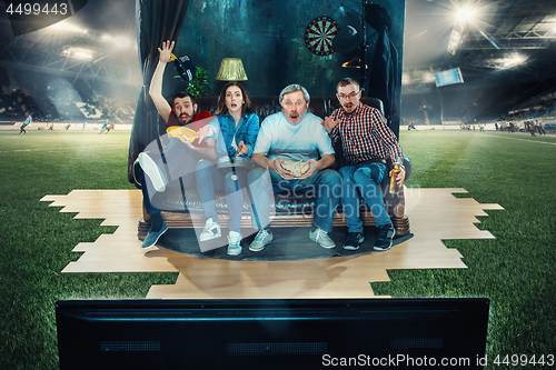 Image of Soccer football fans sitting on the sofa and watching TV in the middle of a football field.