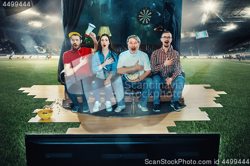 Image of Soccer football fans sitting on the sofa and watching TV in the middle of a football field.
