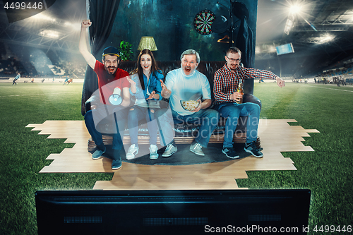 Image of Soccer football fans sitting on the sofa and watching TV in the middle of a football field.