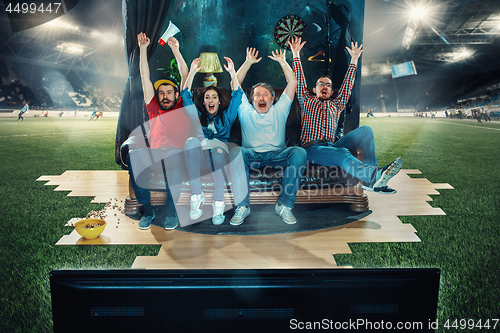 Image of Soccer football fans sitting on the sofa and watching TV in the middle of a football field.