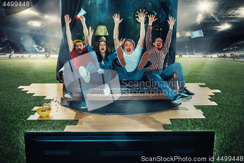 Image of Soccer football fans sitting on the sofa and watching TV in the middle of a football field.