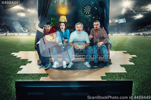 Image of Soccer football fans sitting on the sofa and watching TV in the middle of a football field.