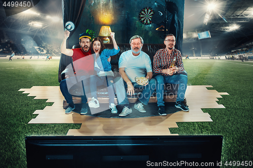 Image of Soccer football fans sitting on the sofa and watching TV in the middle of a football field.