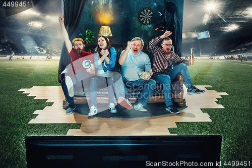 Image of Soccer football fans sitting on the sofa and watching TV in the middle of a football field.