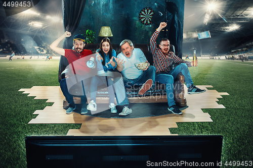 Image of Soccer football fans sitting on the sofa and watching TV in the middle of a football field.