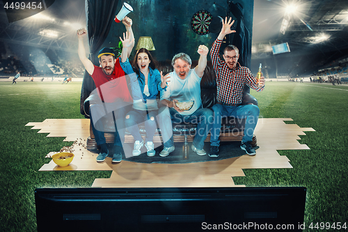 Image of Soccer football fans sitting on the sofa and watching TV in the middle of a football field.