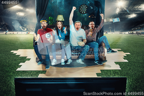 Image of Soccer football fans sitting on the sofa and watching TV in the middle of a football field.