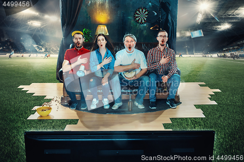 Image of Soccer football fans sitting on the sofa and watching TV in the middle of a football field.