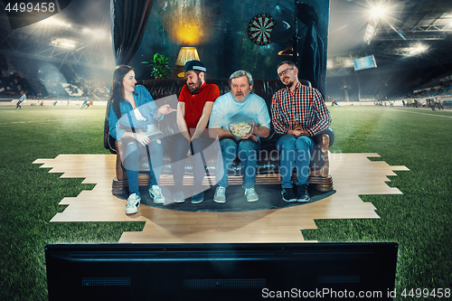 Image of Soccer football fans sitting on the sofa and watching TV in the middle of a football field.