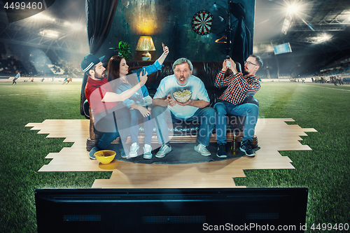 Image of Soccer football fans sitting on the sofa and watching TV in the middle of a football field.