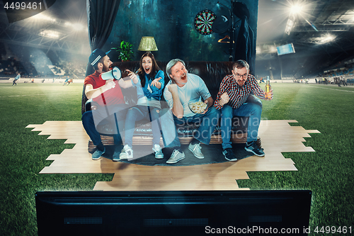 Image of Soccer football fans sitting on the sofa and watching TV in the middle of a football field.