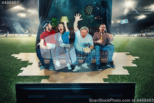 Image of Soccer football fans sitting on the sofa and watching TV in the middle of a football field.