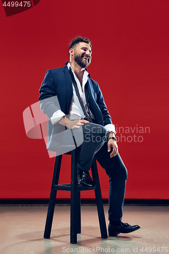 Image of The happy business man sitting and smiling against red background.