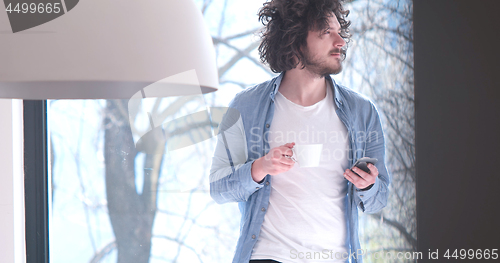 Image of young man drinking coffee and using a mobile phone  at home