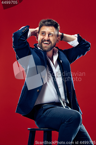 Image of The happy business man sitting and smiling against red background.