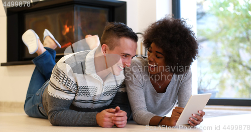 Image of multiethnic couple using tablet computer on the floor