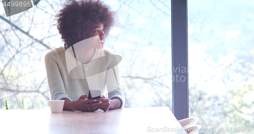 Image of black woman drinking coffee and using a mobile phone  at home