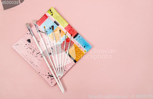 Image of Colorful ceramic plate and paintbrushes on pink background