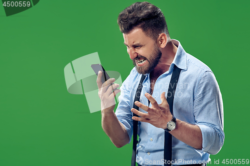 Image of The young emotional angry man screaming on green studio background