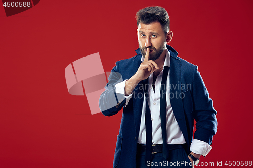 Image of The young man whispering a secret behind her hand over red background