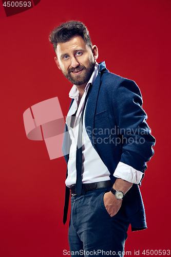 Image of Male beauty concept. Portrait of a fashionable young man with stylish haircut wearing trendy suit posing over red background.