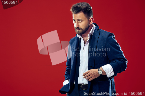 Image of Male beauty concept. Portrait of a fashionable young man with stylish haircut wearing trendy suit posing over red background.