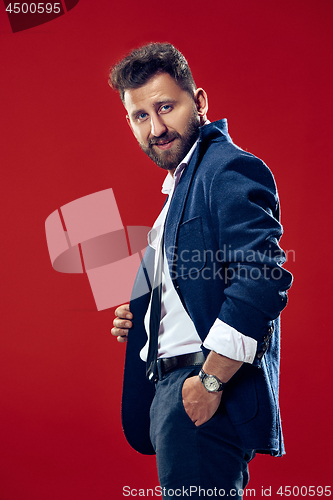 Image of Male beauty concept. Portrait of a fashionable young man with stylish haircut wearing trendy suit posing over red background.