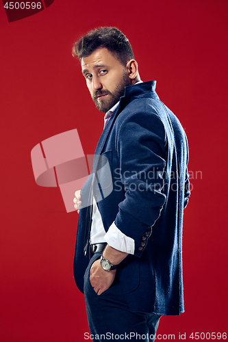 Image of Male beauty concept. Portrait of a fashionable young man with stylish haircut wearing trendy suit posing over red background.