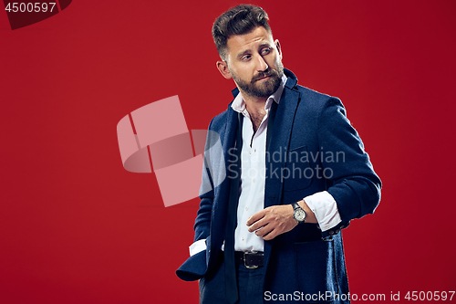 Image of Male beauty concept. Portrait of a fashionable young man with stylish haircut wearing trendy suit posing over red background.