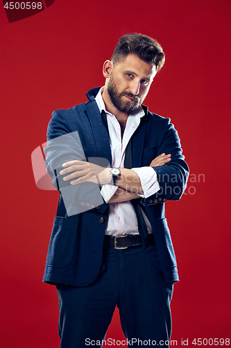 Image of Male beauty concept. Portrait of a fashionable young man with stylish haircut wearing trendy suit posing over red background.