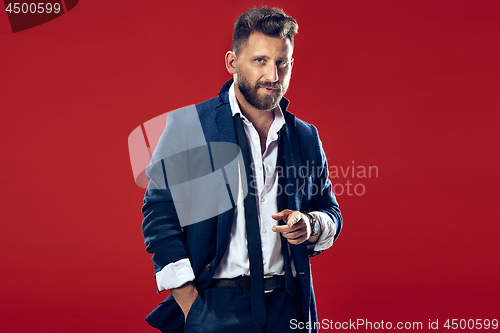 Image of Male beauty concept. Portrait of a fashionable young man with stylish haircut wearing trendy suit posing over red background.